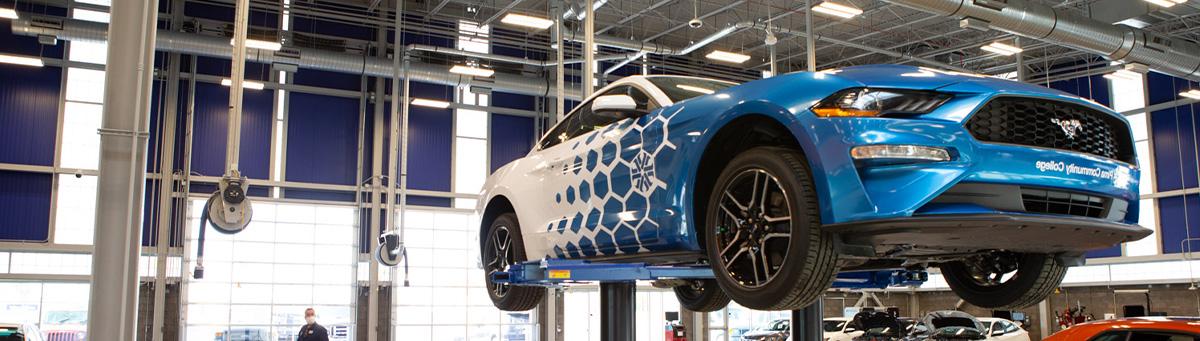 A student in automotive program poses and smiles while working on a vehicle on a lift