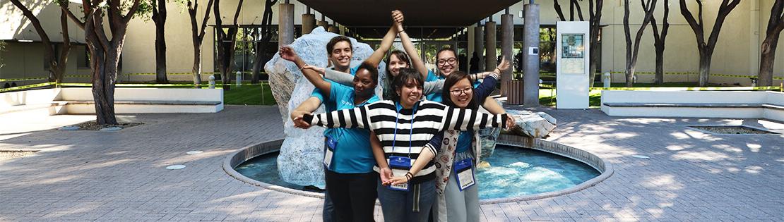 Connect U Students stand in front of the fountain at Pima's Downtown campus posing